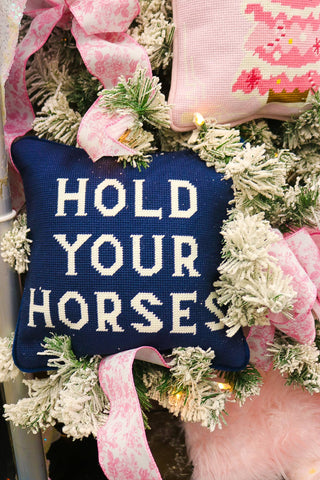 Decorative pillow with 'Hold Your Horses' text on a Christmas wreath with pink ribbons.