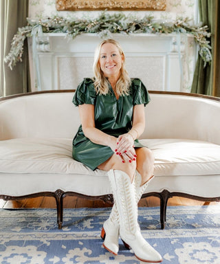 Woman in a green dress and white knee-high boots sitting on a white couch with a decorated fireplace in the background. Whatsoever Things | Dallas, TX | Personalized Apparel and Home Decor for Women and Children 