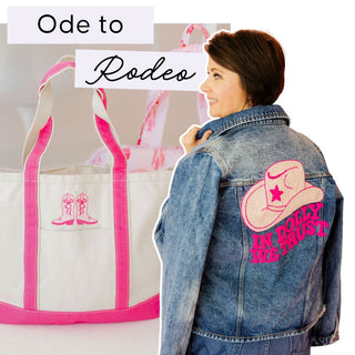 Woman wearing a denim jacket with a pink cowboy hat design and text, next to a tote bag with pink boot designs. | Whatsoever Things | DAllas, TX